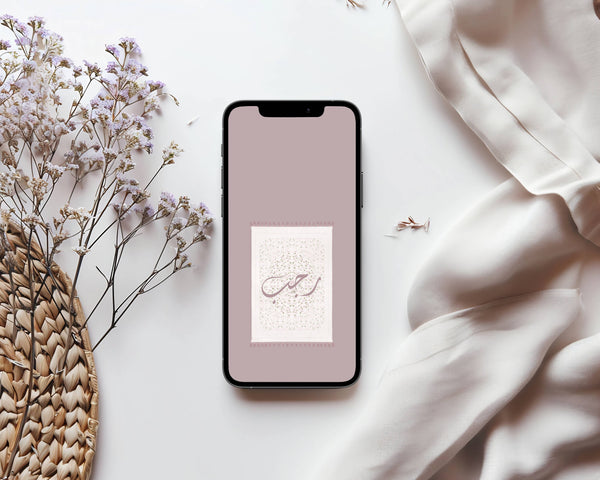 Smartphone with a floral design on a light surface with flowers and fabric. Featuring Rajab Arabic calligraphy over design. 
