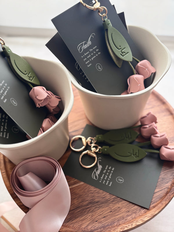 Iman floral keychains resting in plant pots on wooden surface. lifestyle image. Petals of Faith